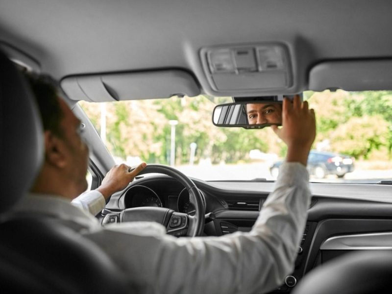 Driver adjusting the rear-view mirror inside a rental car before departure
