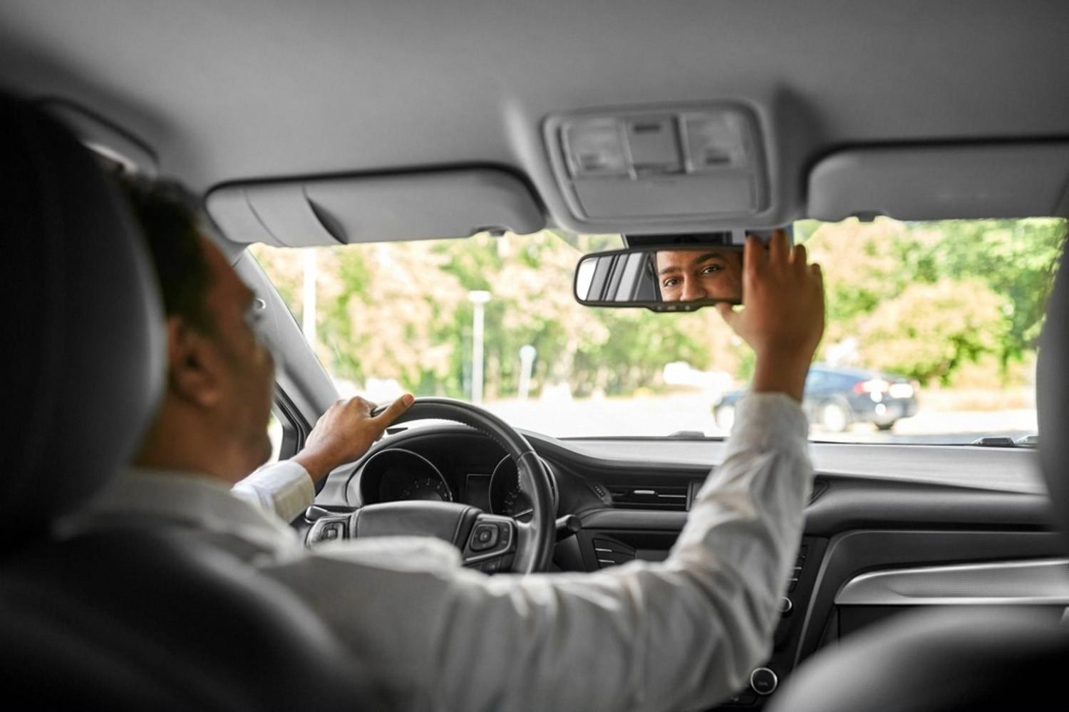 Driver adjusting the rear-view mirror inside a rental car before departure
